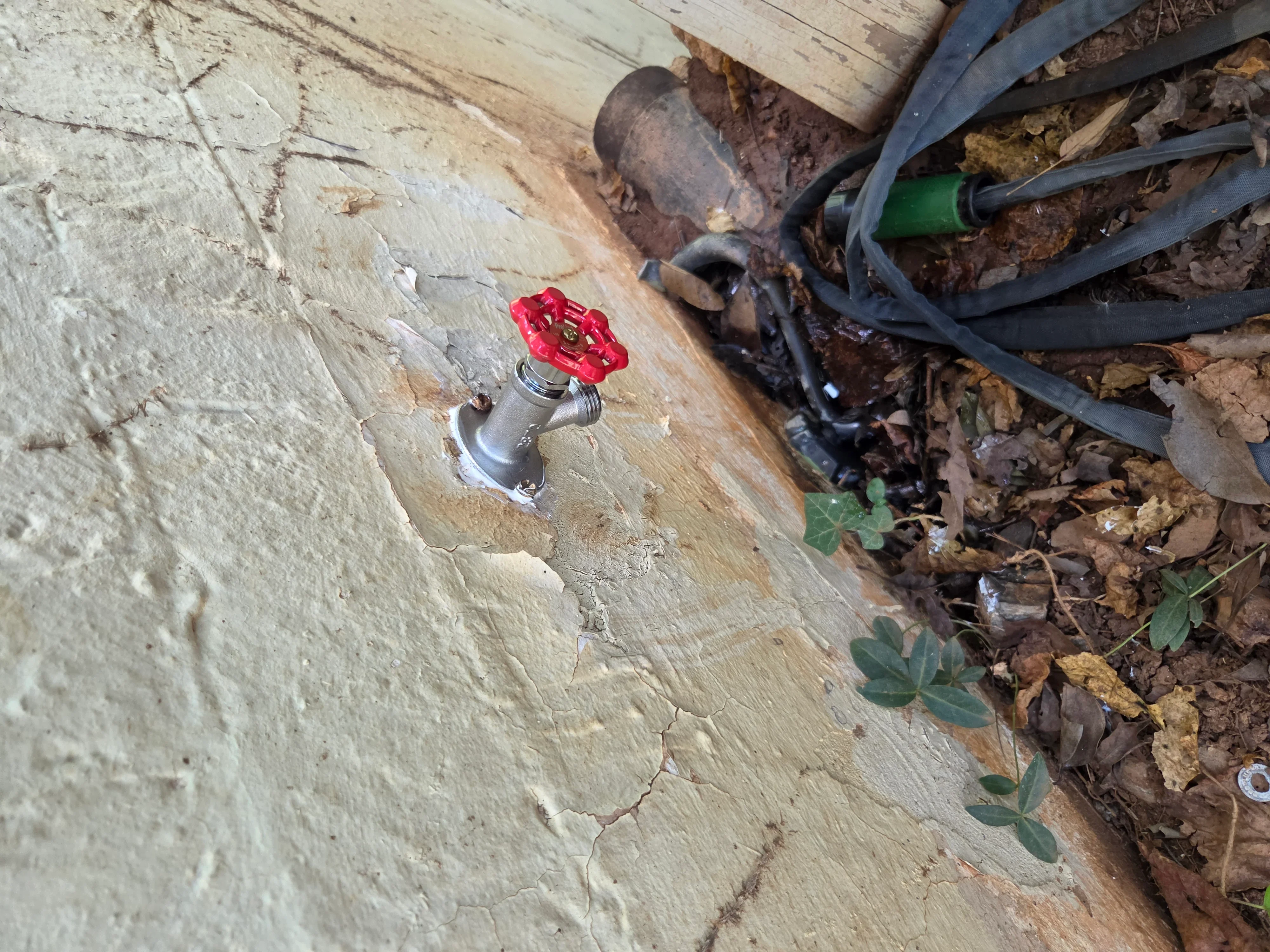 Red ball valve spigot mounted on concrete foundation with supply lines