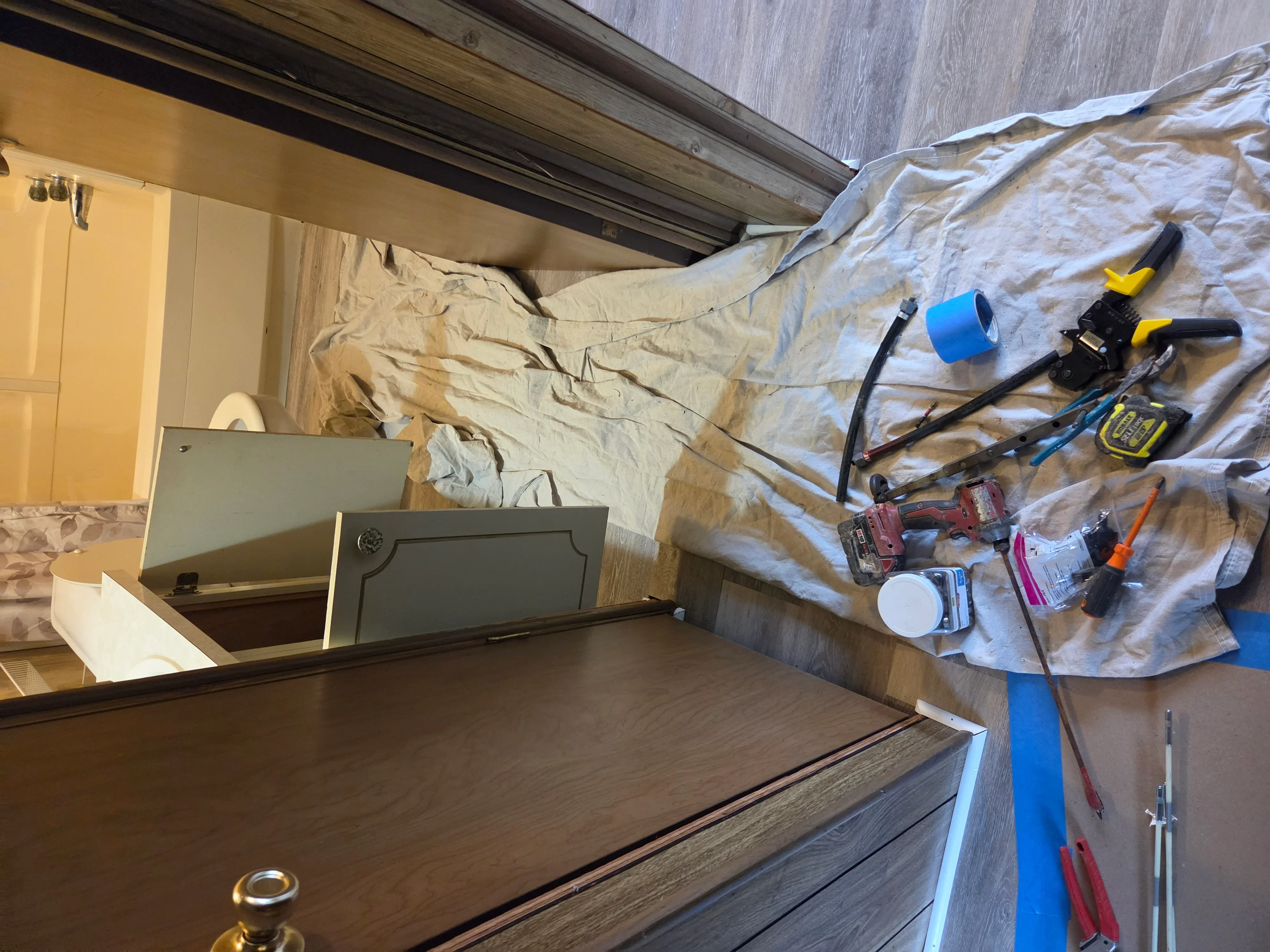 Bathroom vanity cabinet with plumbing supply lines, drain pipes, and installation tools on protective drop cloth