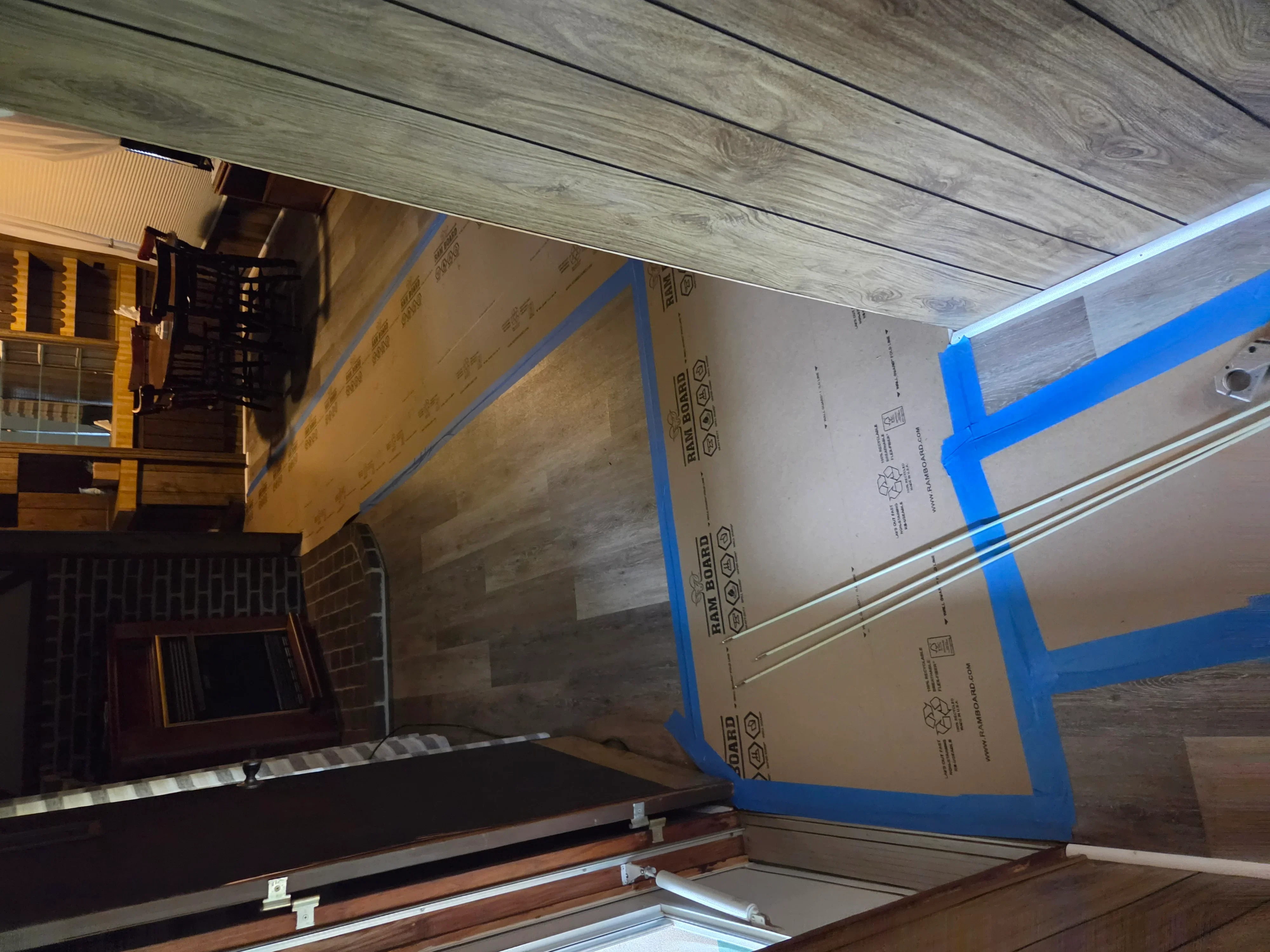 Gray laminate wood-look flooring installation with blue protective tape and metal trim transitions